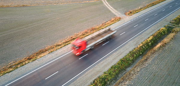 blurry red truck driving on empty road amidst green fields farmland landscape