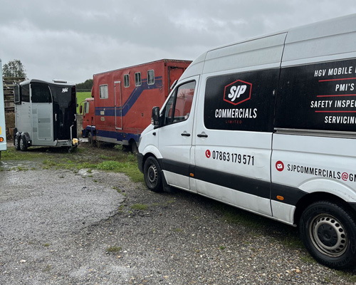 commercial vehicles parked in a gravel area featuring a white van and a trailer with safety inspection equipment