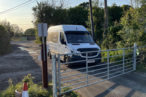 white van parked near a gate in a rural area with greenery surrounding the road