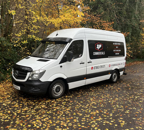 white commercial van parked on a road surrounded by autumn leaves featuring SJP Commercials branding and contact information